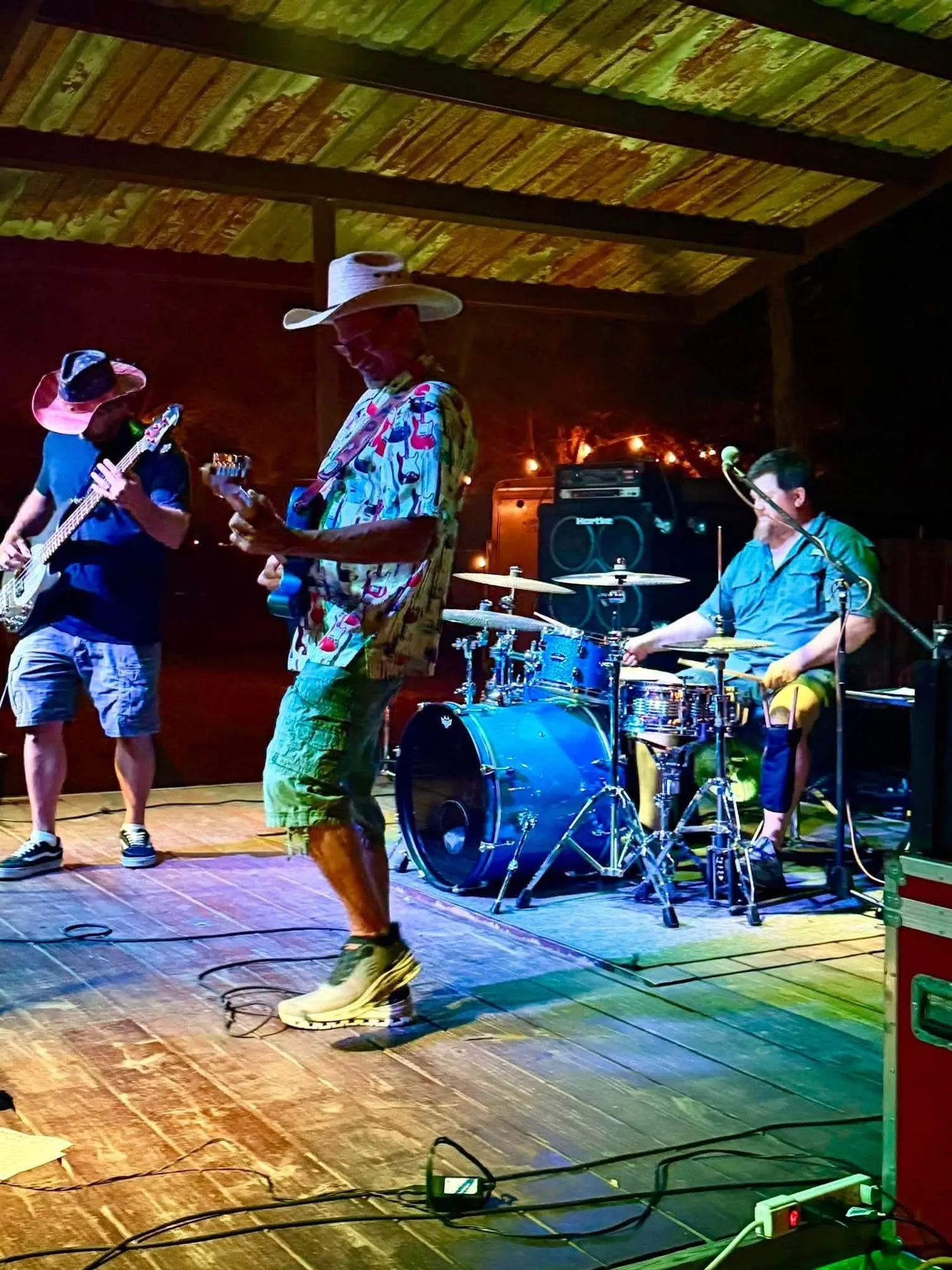 Clay Potter Band trio performing live country music on a rustic covered wooden stage under colorful lights Clay Potter Band trio performing live country music on a rustic covered wooden stage under colorful lights